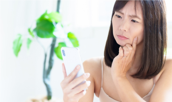 スマホのカメラを見て納得いかない女性の顔です。